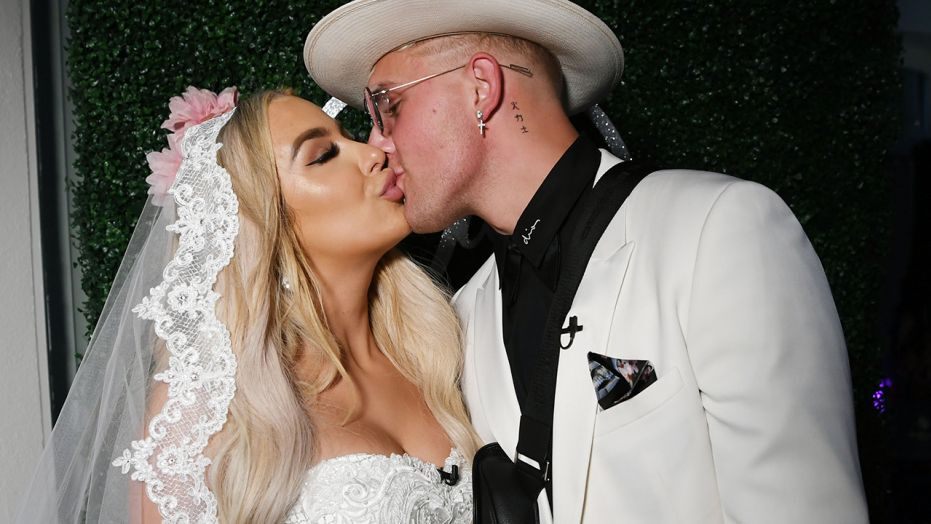 tana in a white wedding gown with jake in a white suit kissing on their wedding day 