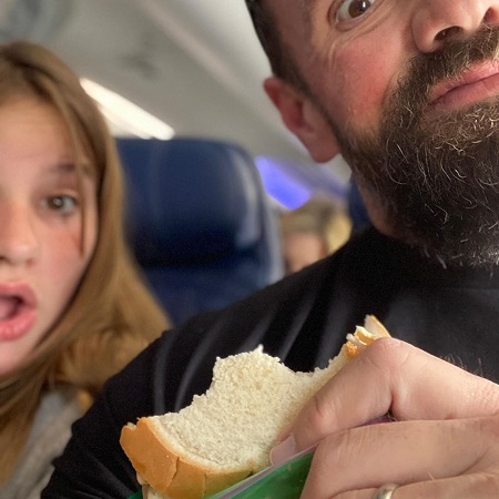 Ethan Suplee holding a sandwich and his daughter gasping beside him in an airplane. Both their faces are not complete.