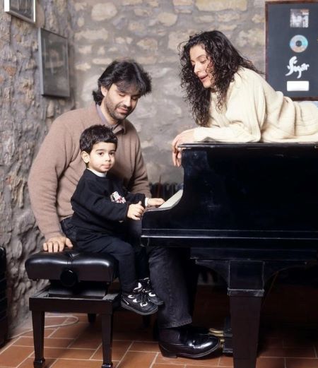 Andrea Bocelli with his first son Amos and his ex-wife Enrica Cenzatti in front of a piano.