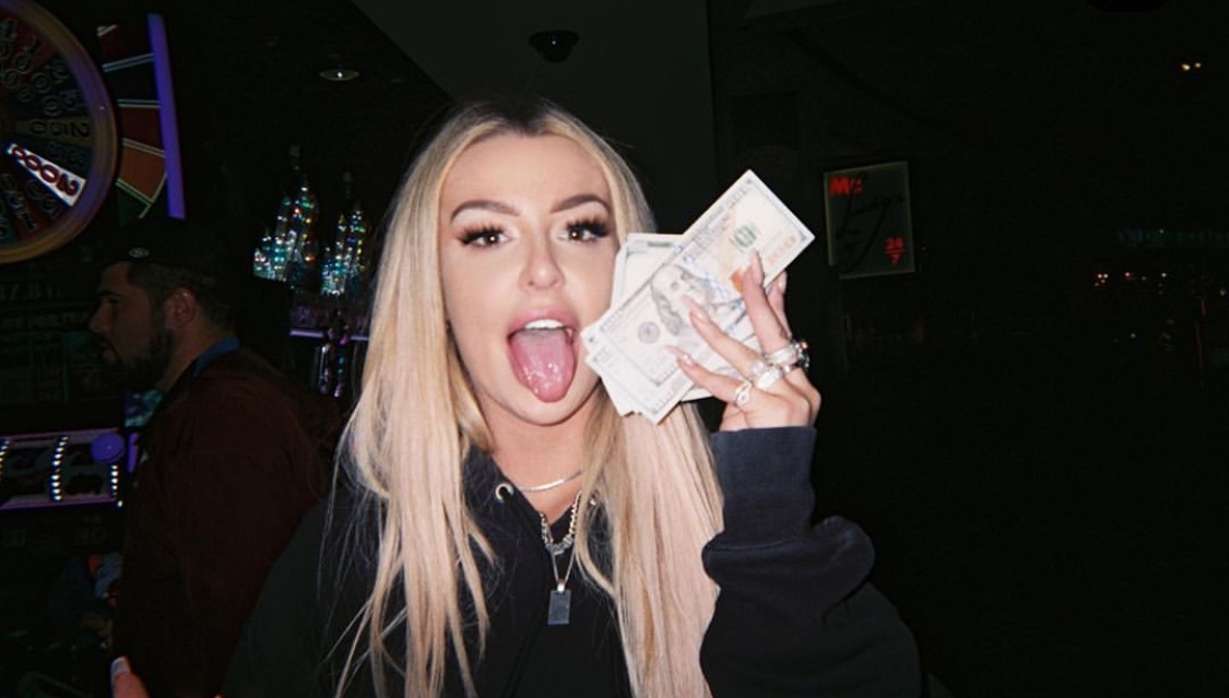 tana golding a wad of money posing for the camera with her tongue out  