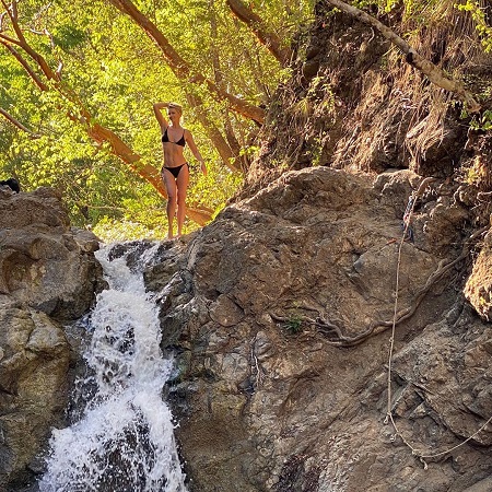 Paulina Porizkova in a black two-piece bikini on top of a waterfall.