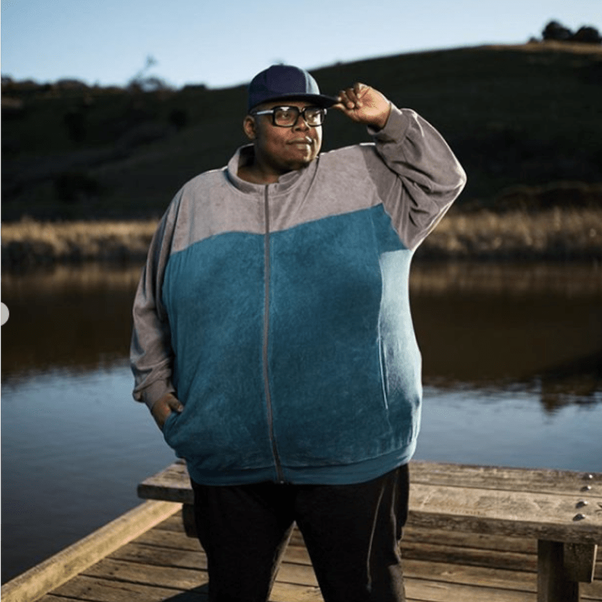 jumoke standing on the lake side wearing a hoodie cap and glasses 