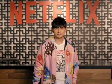 Jay Chou in a pink jacket poses in front of a Netflix wall.