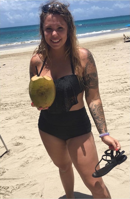 Kailyn Lowry in the beach with a coconut in one hand and a sandal down the other hand.