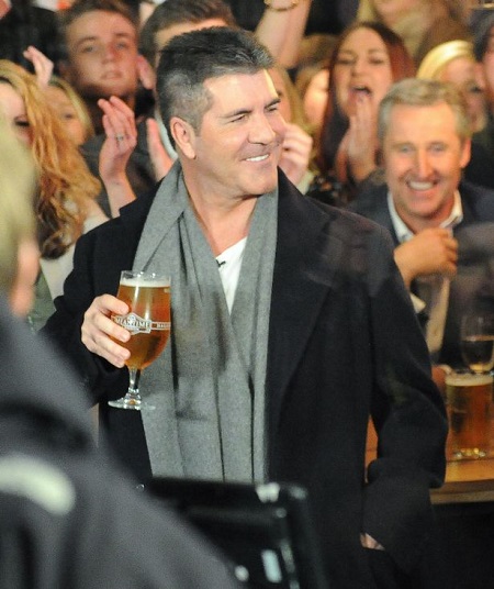 Simon Cowell holding a glass of beer in public and smiling at the crowd.