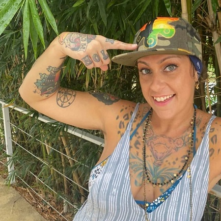 Danielle Colby pointing to her hat while smiling in front of railings.