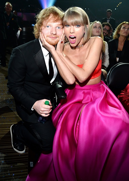 Taylor Swift holding Ed Sheeran's face with a surprised looked on her own face.